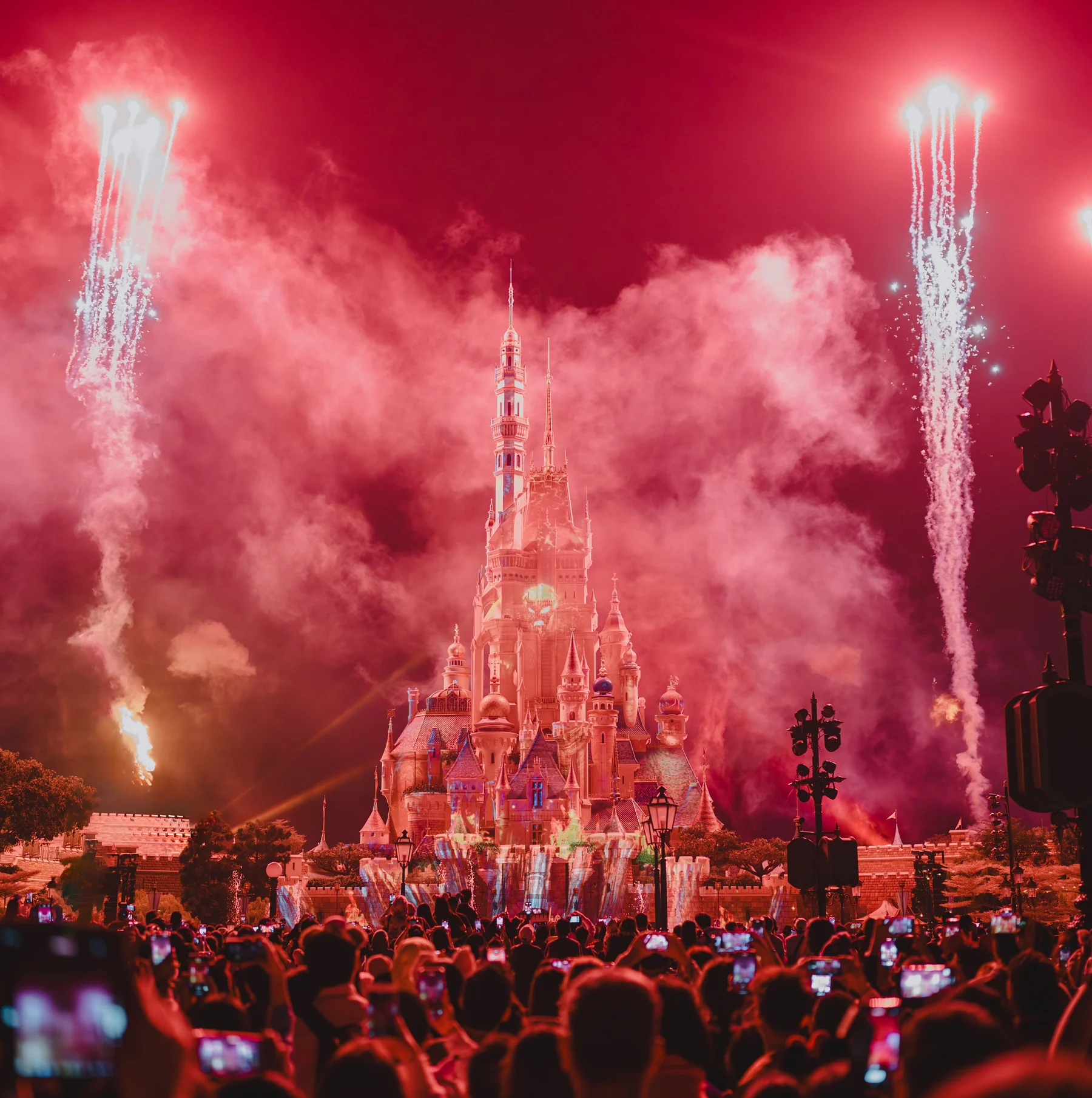 Fuegos artificiales sobre un castillo iluminado y una multitud con los teléfonos en alto