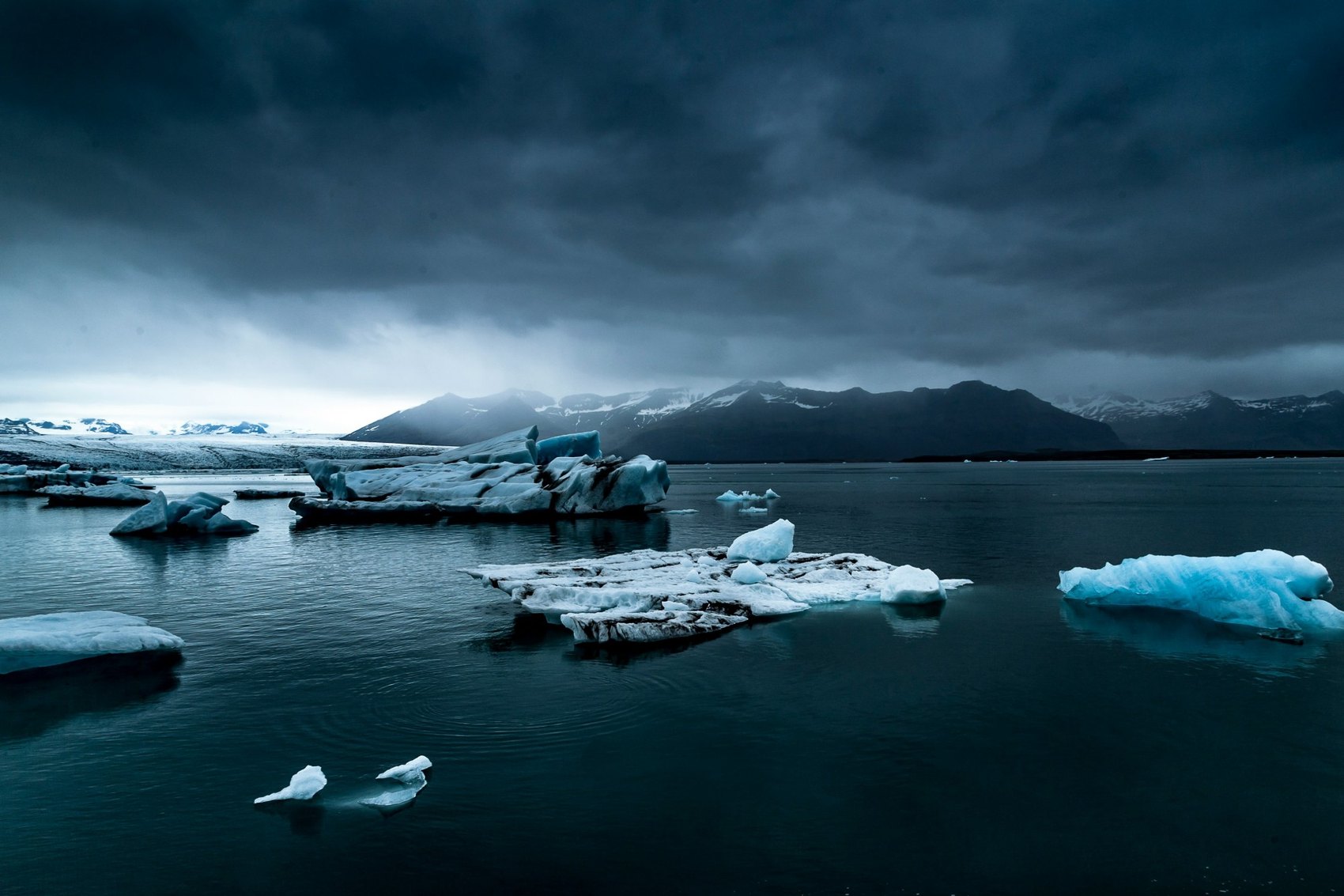 La laguna glaciar de Jökulsárlón bajo un cielo de tormenta: témpanos de hielo azul flotando frente a la lengua del glaciar y las montañas nevadas